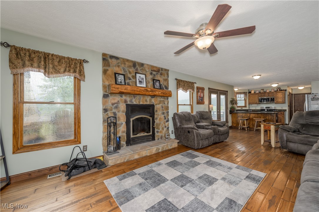 9715 Williams Road Diamond, OH 44412 - Photo 38 of 48 Living room with a stone fireplace, a textured ceiling, hardwood / wood-style flooring, and ceiling fan