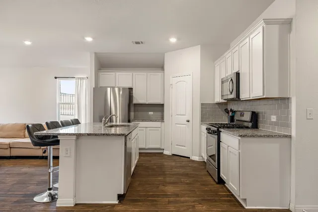 a kitchen with stainless steel appliances granite countertop a stove top oven a refrigerator a sink and dishwasher with wooden floor