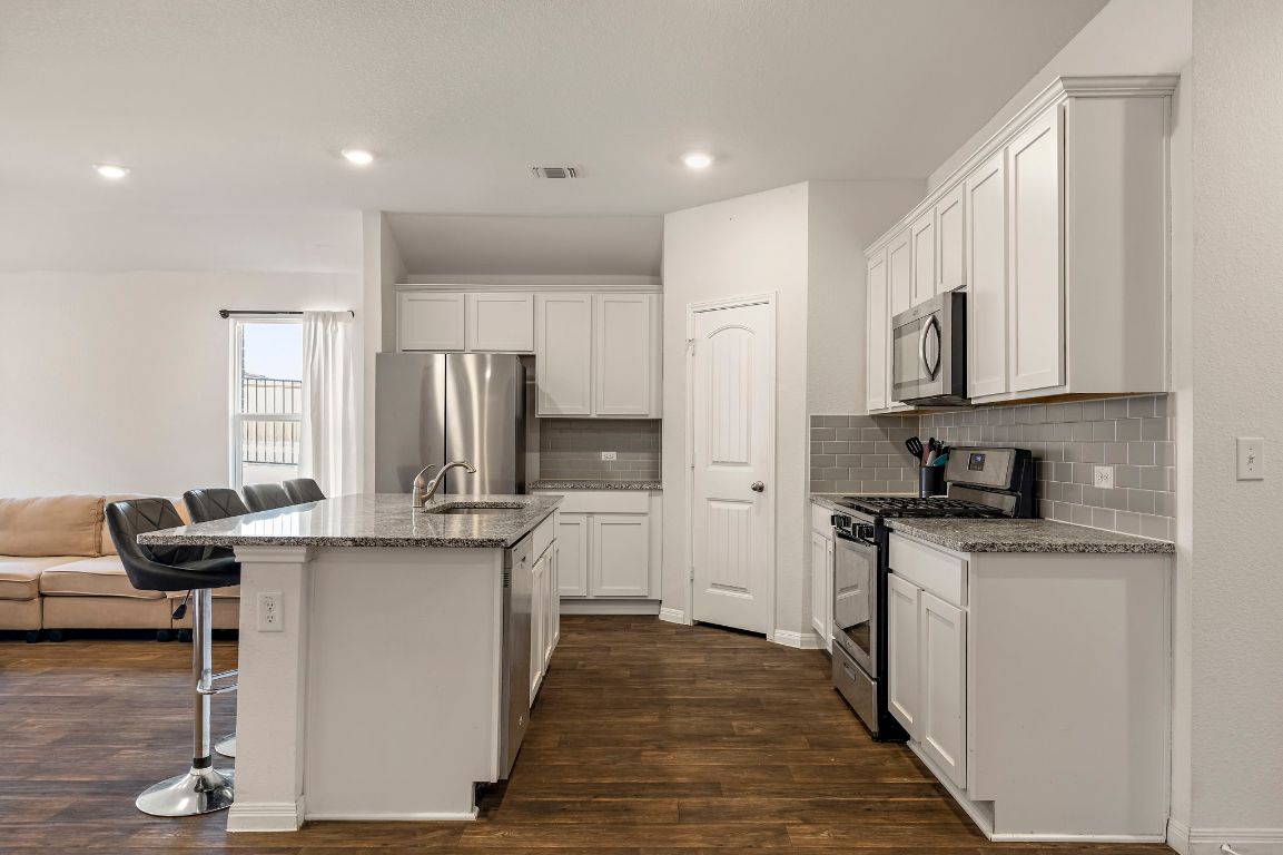 19601 Abigail Fillmore Road Manor, TX 78653 - Photo 6 of 17 a kitchen with stainless steel appliances granite countertop a stove top oven a refrigerator a sink and dishwasher with wooden floor