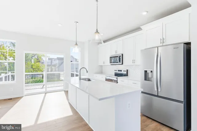 a kitchen with stainless steel appliances a refrigerator a sink dishwasher a oven and white cabinets with wooden floor