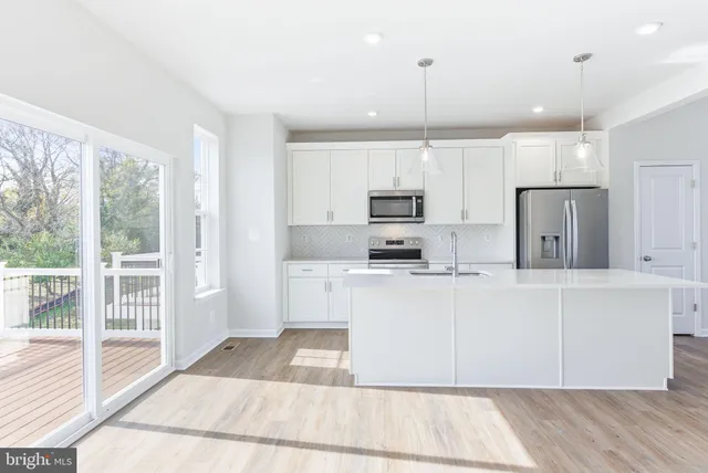 a kitchen with stainless steel appliances kitchen island granite countertop a refrigerator a sink a stove and white cabinets with wooden floor