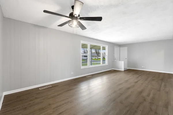 an empty room with wooden floor fan and windows