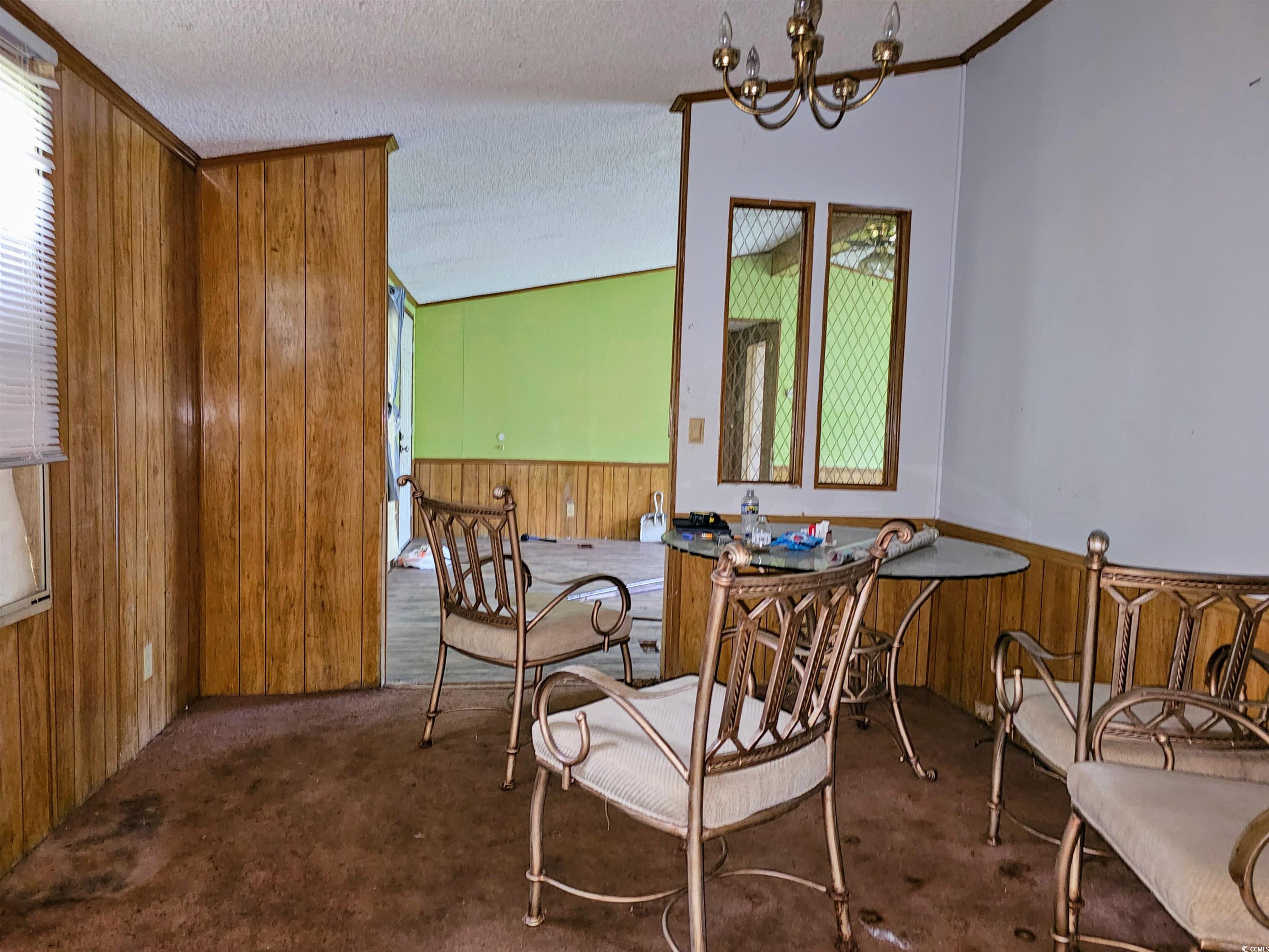 827 1/2 North Firetower Road Florence, SC 29506 - Photo 9 of 29 Carpeted dining room featuring wooden walls, wainscoting, plenty of natural light, a textured ceiling, and a chandelier