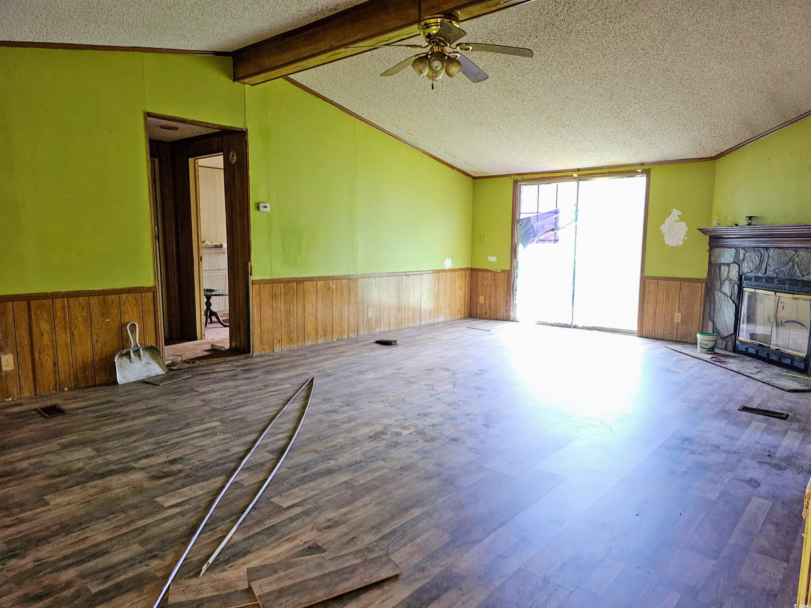 827 1/2 North Firetower Road Florence, SC 29506 - Photo 10 of 29 Unfurnished living room with a textured ceiling, wainscoting, wood finished floors, a stone fireplace, and wooden walls