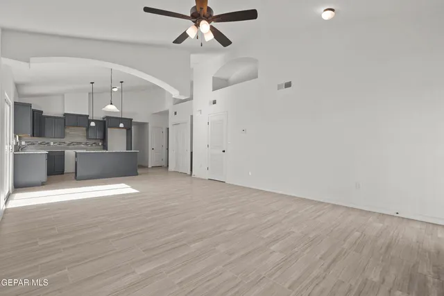 an empty room with wooden floor ceiling fan and kitchen view