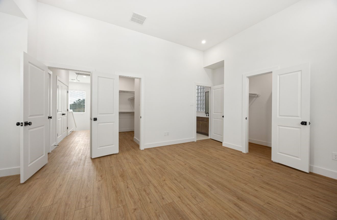 2121 Hoskins Drive, Unit C Houston, TX 77080 - Photo 24 of 34 Large bedroom suite with high ceilings, wood-look flooring, crisp white walls, and multiple access points to closets and bath areas. The open layout provides excellent flexibility, while the clean modern finishes, black hardware, and abundant storage create a polished and practical private retreat.