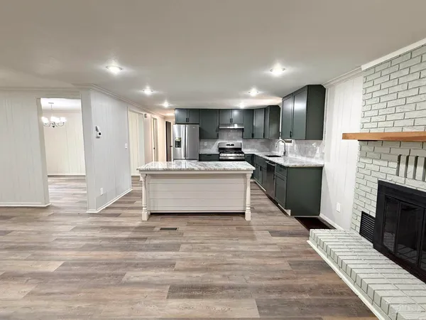 a living room with stainless steel appliances kitchen island granite countertop a sink dishwasher a stove and a kitchen island with wooden floor