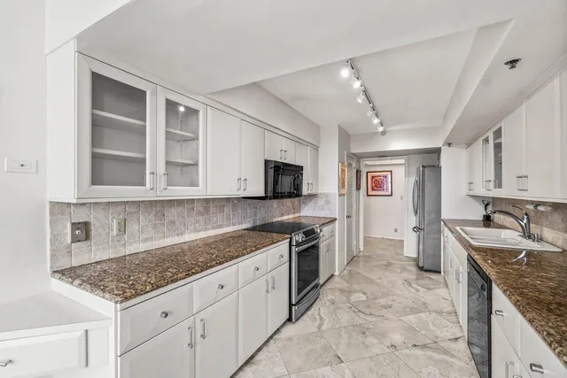 a kitchen with stainless steel appliances granite countertop a stove top oven a sink a dining table and chairs with white cabinets