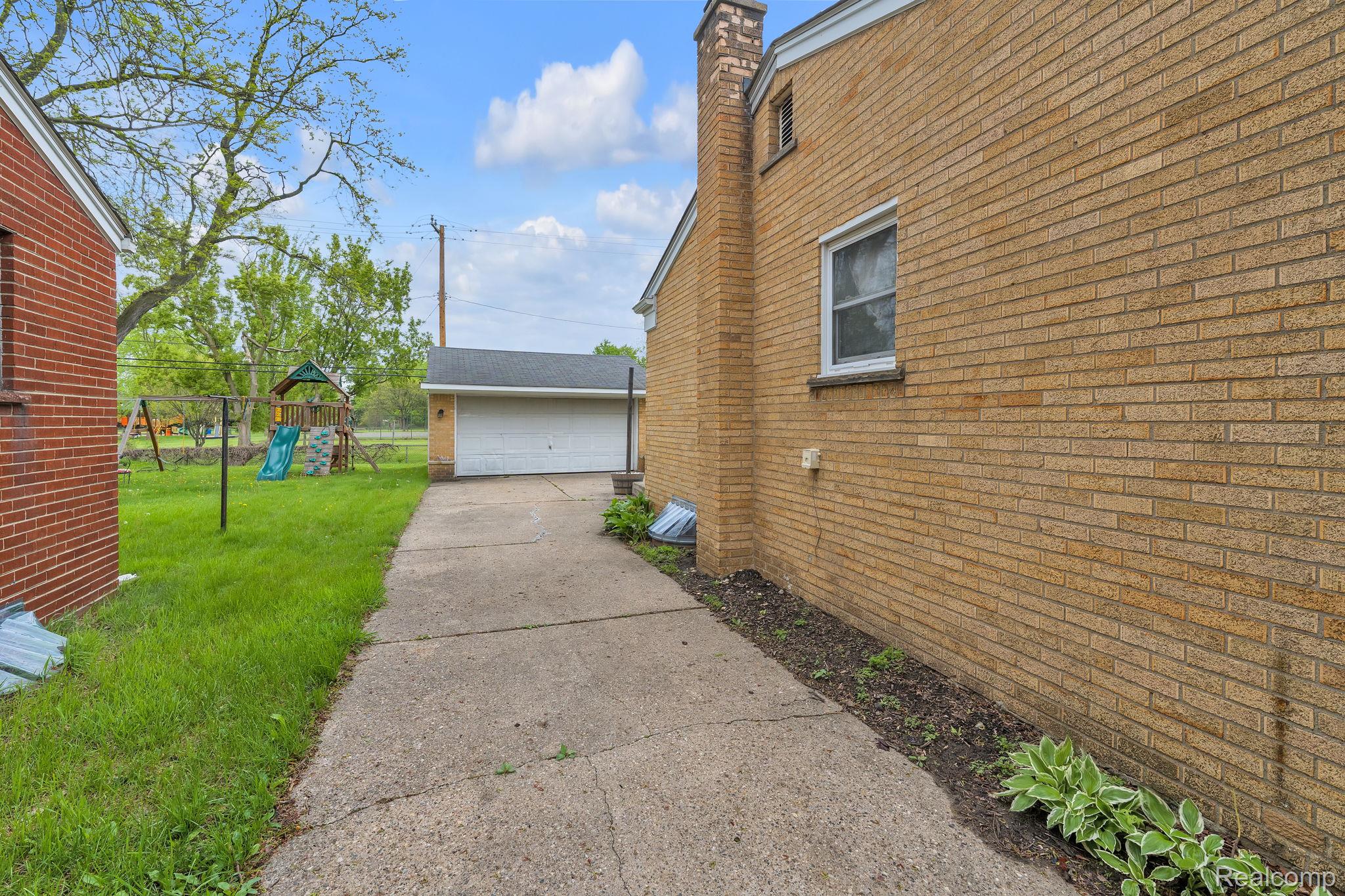 37022 Pinewood Road Wayne, MI 48184 - Photo 25 of 30 View of side of home featuring a garage, an outbuilding, a yard, brick siding, and a chimney