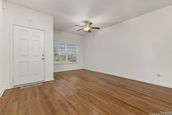 an empty room with wooden floor chandelier fan and windows