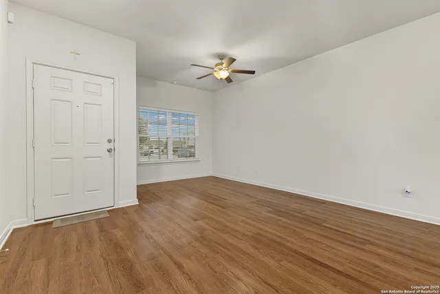 an empty room with wooden floor chandelier fan and windows
