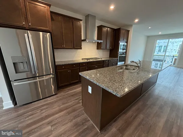 a kitchen with stainless steel appliances granite countertop a refrigerator a sink dishwasher a stove and white countertops with wooden floor