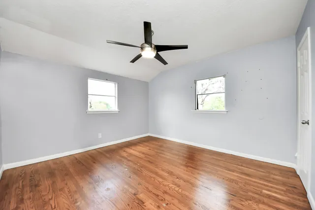 a view of empty room with wooden floor and fan