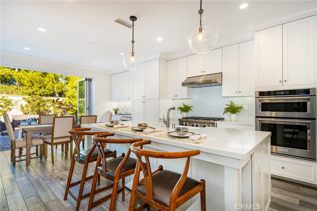 57 Bandana Irvine, CA 92602 - Photo 5 of 32 a kitchen with stainless steel appliances kitchen island granite countertop a stove a sink a dining table and chairs with the wooden floor