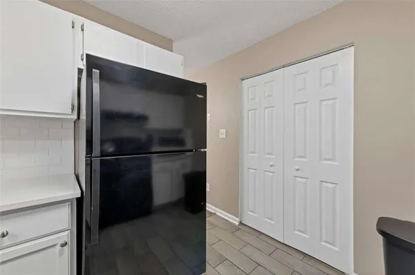 a view of a refrigerator in kitchen and an empty room with wooden floor