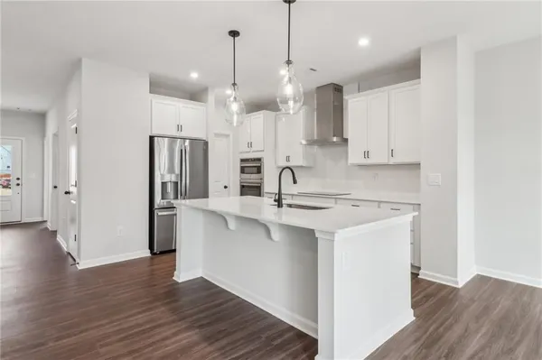 a kitchen with stainless steel appliances a refrigerator a sink dishwasher a stove and white cabinets with wooden floor