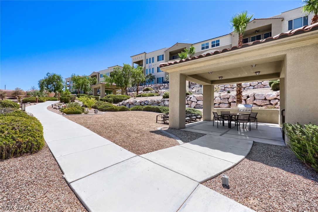 2555 Hampton Road, Unit 9301 Henderson, NV 89052 - Photo 33 of 36 A winding pathway guides through meticulously landscaped grounds, leading to a shaded outdoor dining area with a grill.