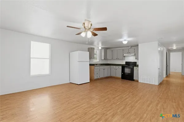 a view of an empty room with window and kitchen view