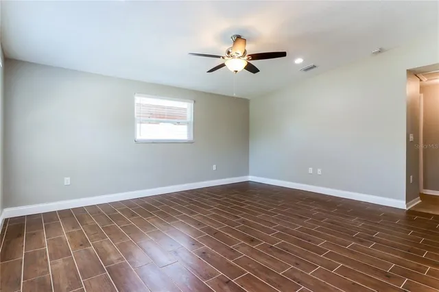 a view of an empty room with wooden floor and a ceiling fan