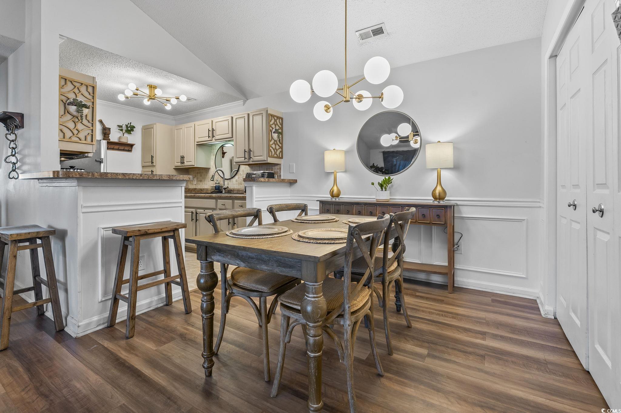 3753 Citation Way, Unit 438 Myrtle Beach, SC 29577 - Photo 5 of 33 Dining room with a chandelier, vaulted ceiling, dark wood-style floors, a textured ceiling, and a wainscoted wall