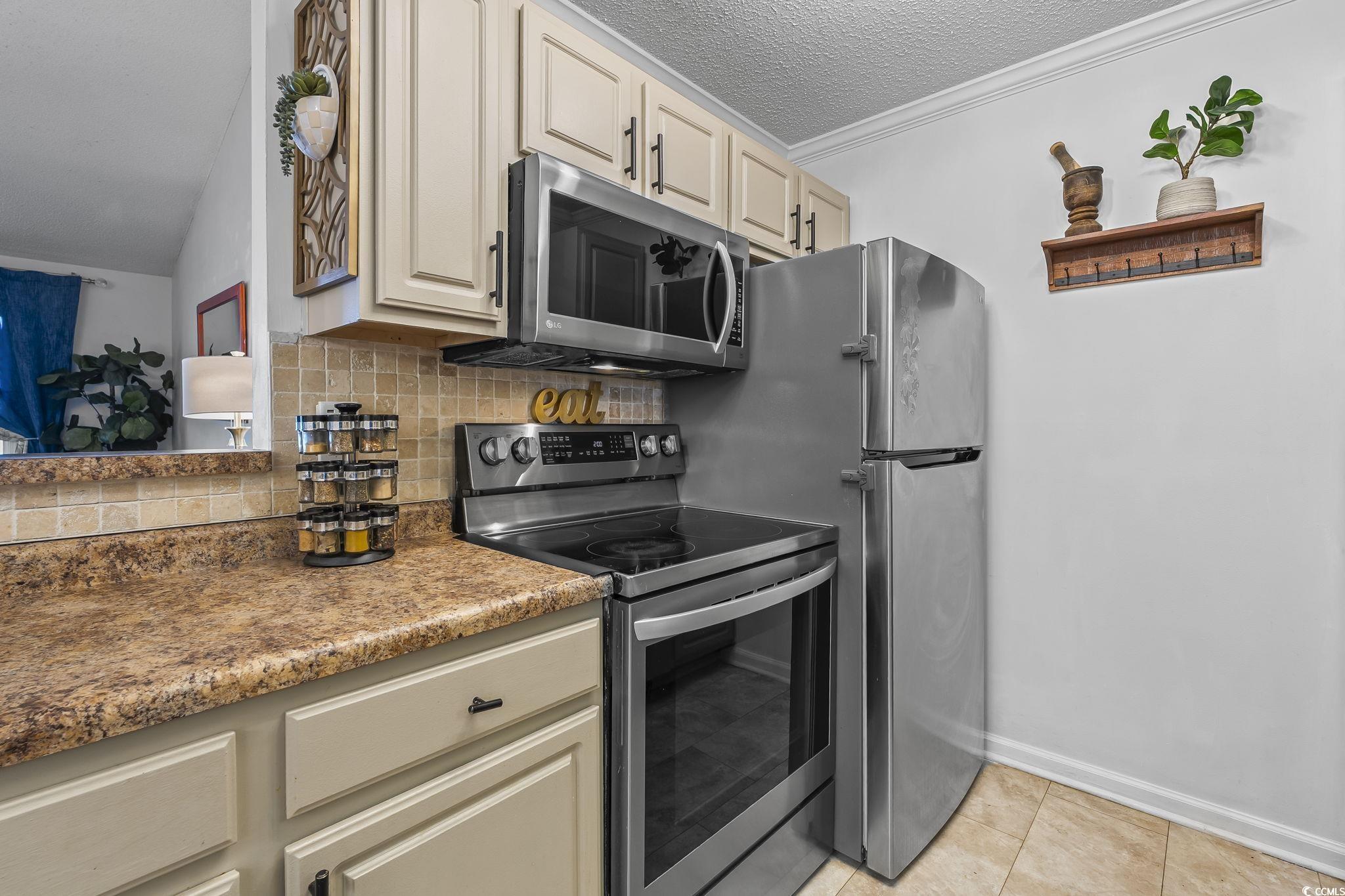 3753 Citation Way, Unit 438 Myrtle Beach, SC 29577 - Photo 8 of 33 Kitchen with stainless steel appliances, decorative backsplash, cream cabinetry, light stone countertops, and a textured ceiling