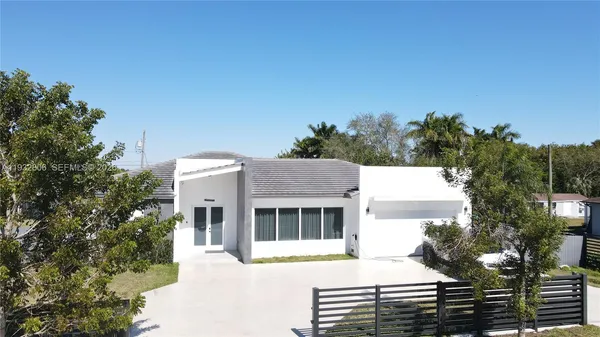a view of a white house with a small yard and large trees
