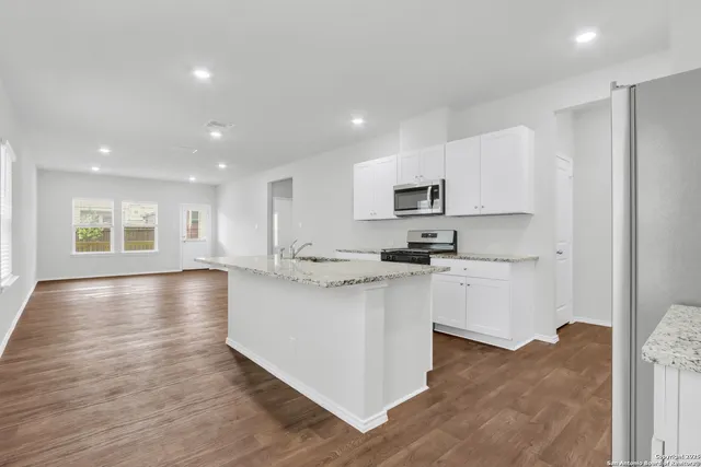 a kitchen with stainless steel appliances granite countertop a stove a sink a refrigerator and white cabinets with wooden floor