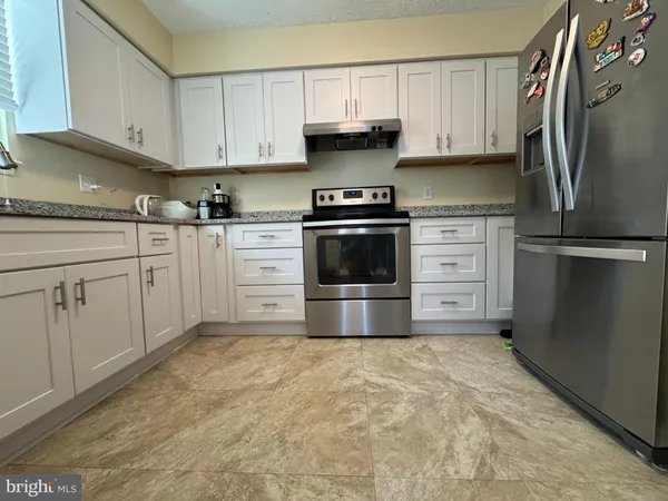a kitchen with granite countertop a refrigerator stove and white cabinets