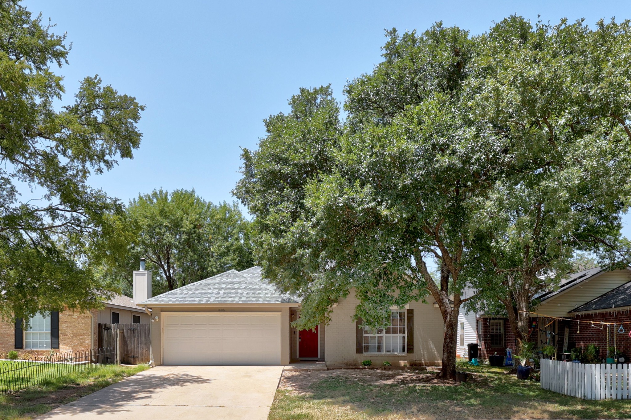 1806 Rusty Nail Loop Round Rock, TX 78681 - Photo 2 of 28 A welcoming facade with a vibrant red door stands shaded by mature, leafy trees, presenting attractive curb appeal.