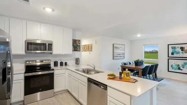 a kitchen with stainless steel appliances kitchen island granite countertop a sink dishwasher stove and white cabinets with wooden floor