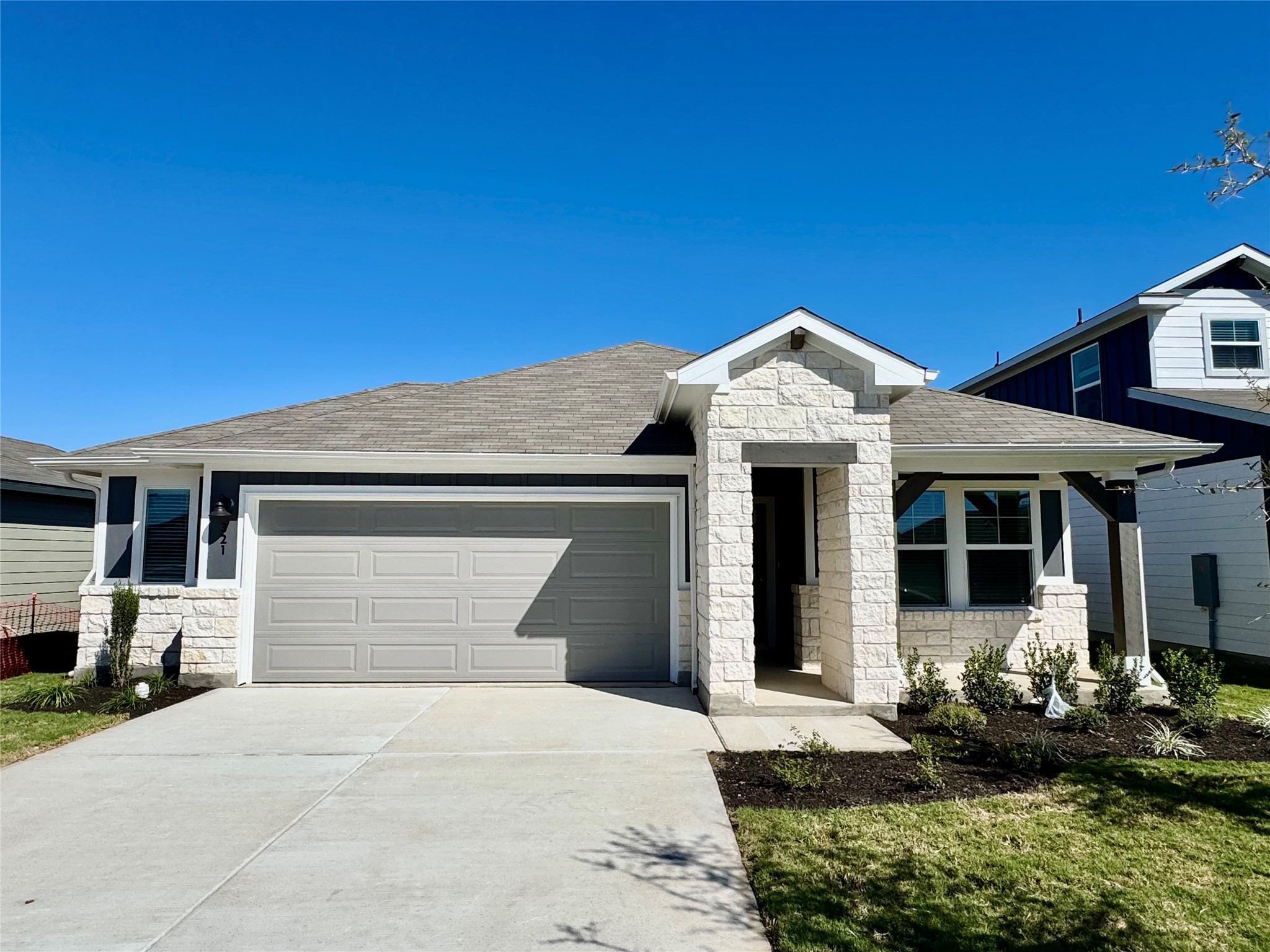 View of front facade with stone siding, roof with shingles, concrete driveway, an attached garage, and a front yard