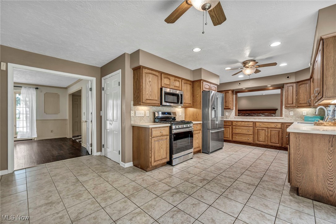 38814 Johnnycake Ridge Road Willoughby, OH 44094 - Photo 16 of 48 Kitchen featuring stainless steel appliances, ceiling fan, a sink, light tile patterned floors, and decorative backsplash