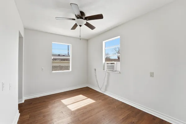 an empty room with wooden floor ceiling fan and windows