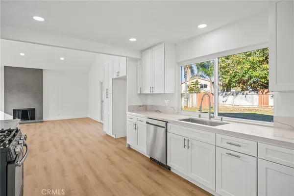 a kitchen with stainless steel appliances granite countertop a stove a sink a refrigerator and white cabinets with wooden floor