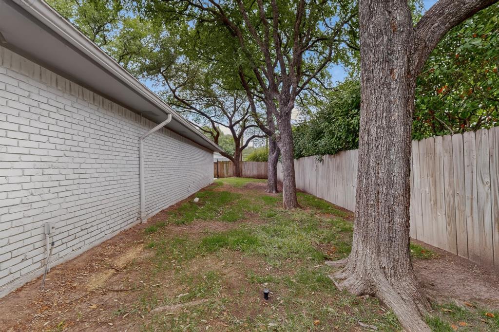 7631 Meadow Road Dallas, TX 75230 - Photo 37 of 40 A tranquil yard lined with trees and a rustic fence, inviting a sense of nature and privacy.