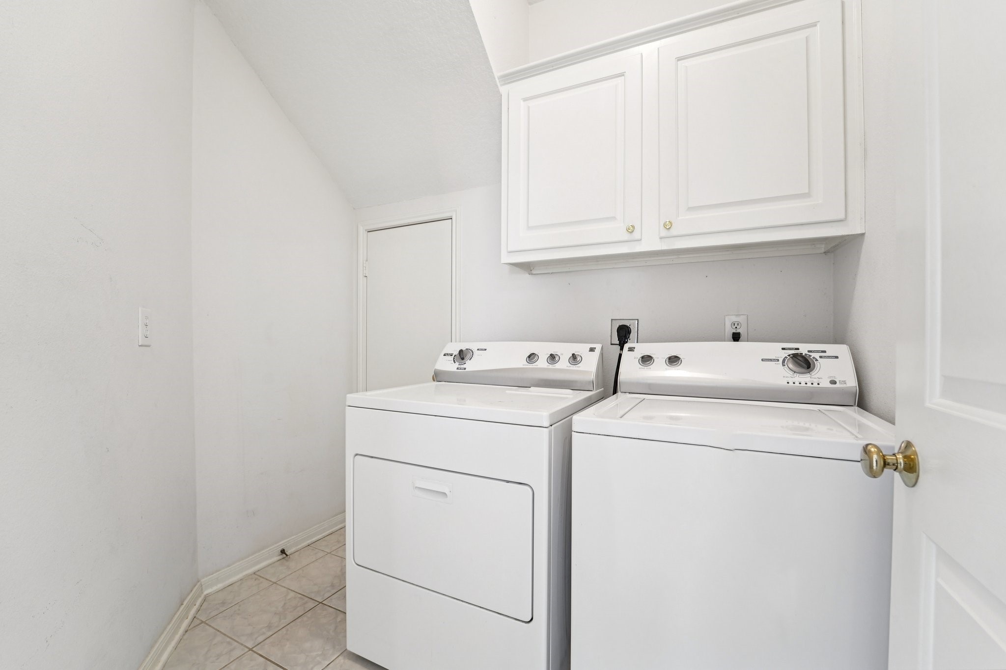 14420 Walters Road, Unit 55 Houston, TX 77014 - Photo 13 of 35 A laundry room featuring a washer and dryer side by side, with white cabinetry above for storage. The space is clean and functional, with tiled flooring and a neutral color scheme.