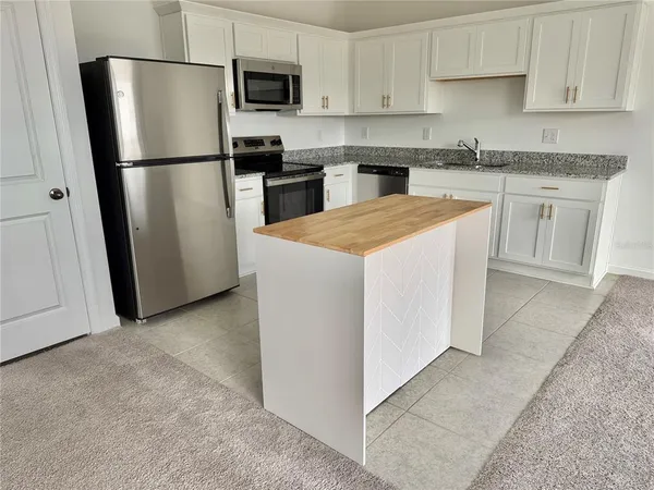 a kitchen with stainless steel appliances granite countertop a refrigerator a stove a sink a microwave a counter space and cabinets