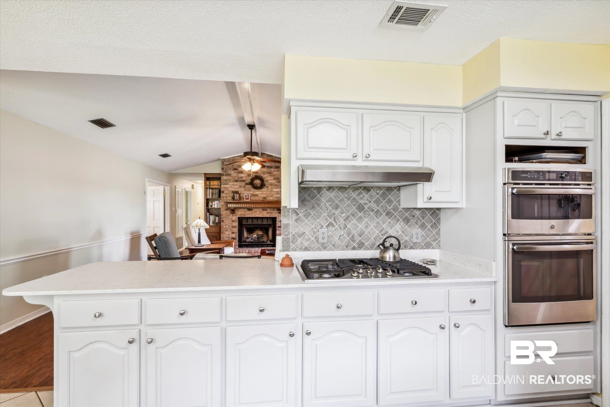 8710 Three Notch Road Mobile, AL 36619 - Photo 9 of 30 Kitchen with appliances with stainless steel finishes, backsplash, a brick fireplace, light hardwood / wood-style flooring, and vaulted ceiling