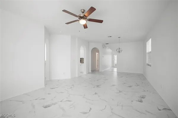an empty room with chandelier fan and windows