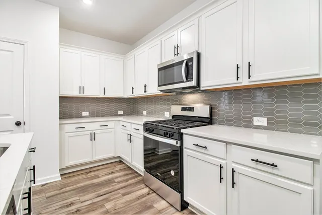 a kitchen with stainless steel appliances granite countertop white cabinets a sink dishwasher and a stove with wooden floor