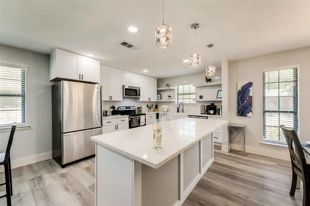 a large white kitchen with a refrigerator a stove a kitchen island and couches with wooden floor