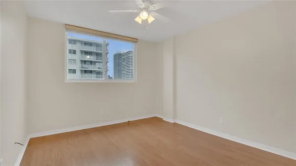 a bedroom with a bed and a lamp on dresser with wooden floor