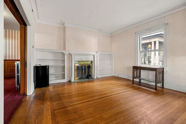 a view of an empty room with wooden floor fireplace and a window