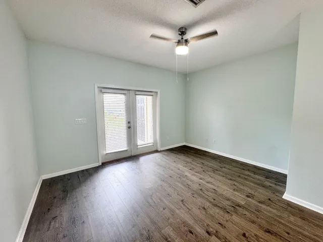an empty room with wooden floor chandelier fan and windows