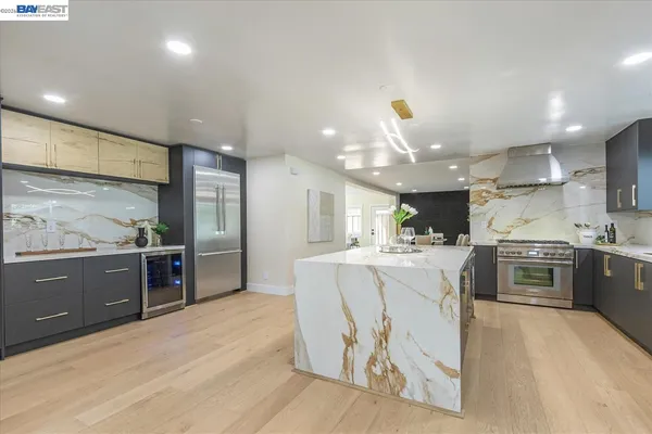 a large kitchen with stainless steel appliances kitchen island granite countertop a large kitchen island a stove a refrigerator a sink a dining table and chairs with wooden floor