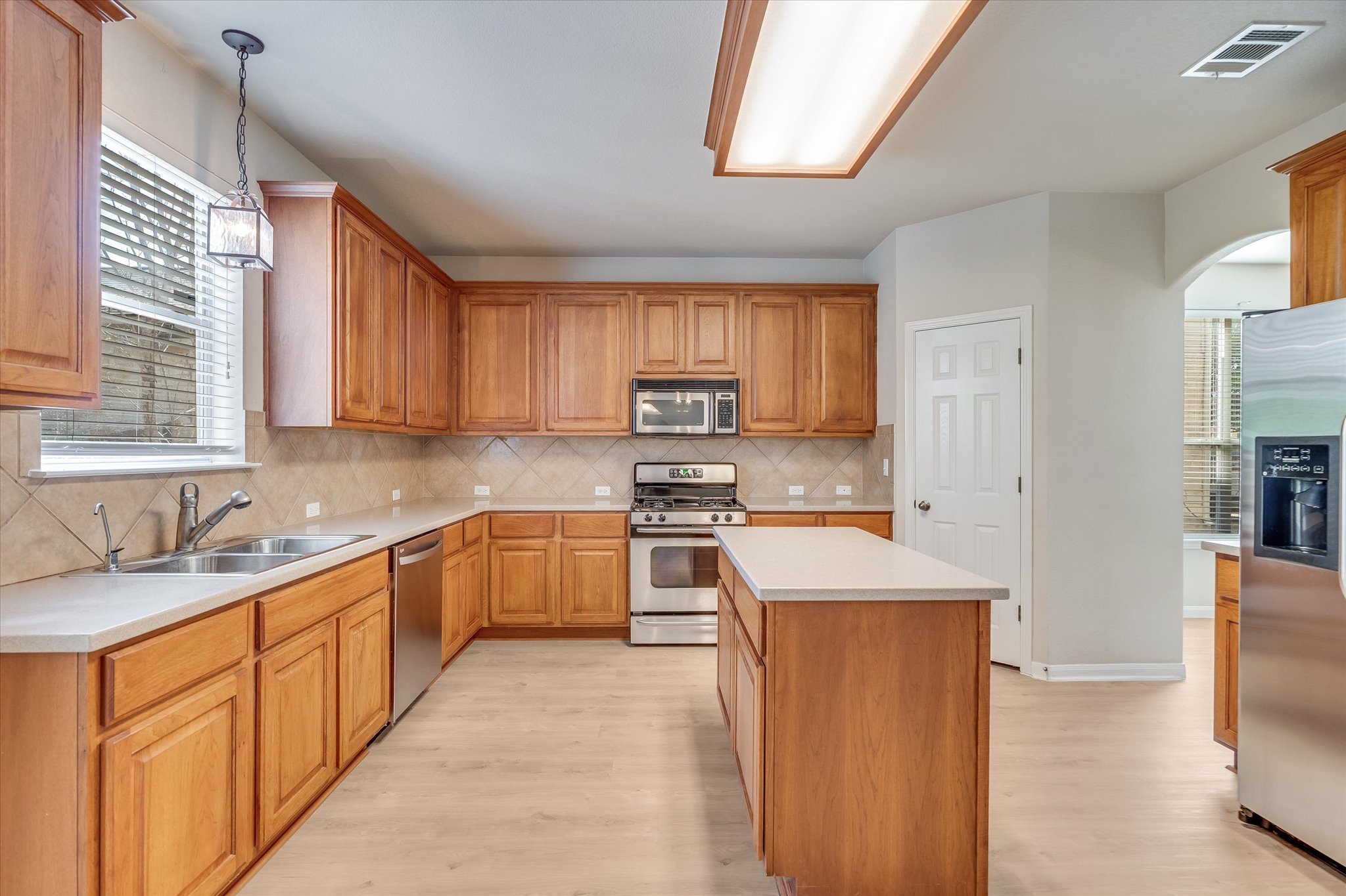 4029 Lake Edge Way Pflugerville, TX 78660 - Photo 9 of 35 Kitchen featuring stainless steel appliances, light countertops, light wood-style floors, arched walkways, and a kitchen island