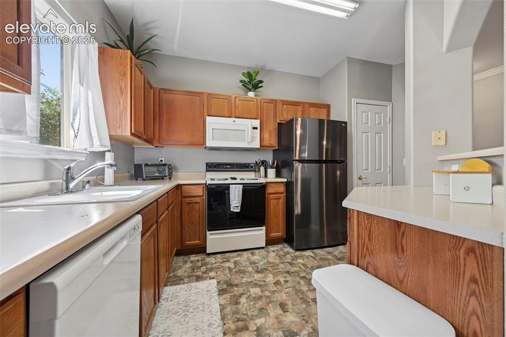 3715 Riviera Grove, Unit 101 Colorado Springs, CO 80922 - Photo 14 of 36 Kitchen featuring wood cabinetry, light-toned countertops, a stainless steel refrigerator, and a white oven/range with an overhead microwave