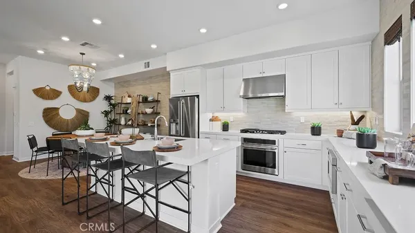 a kitchen with stainless steel appliances kitchen island granite countertop a stove a sink a refrigerator and white cabinets with wooden floor