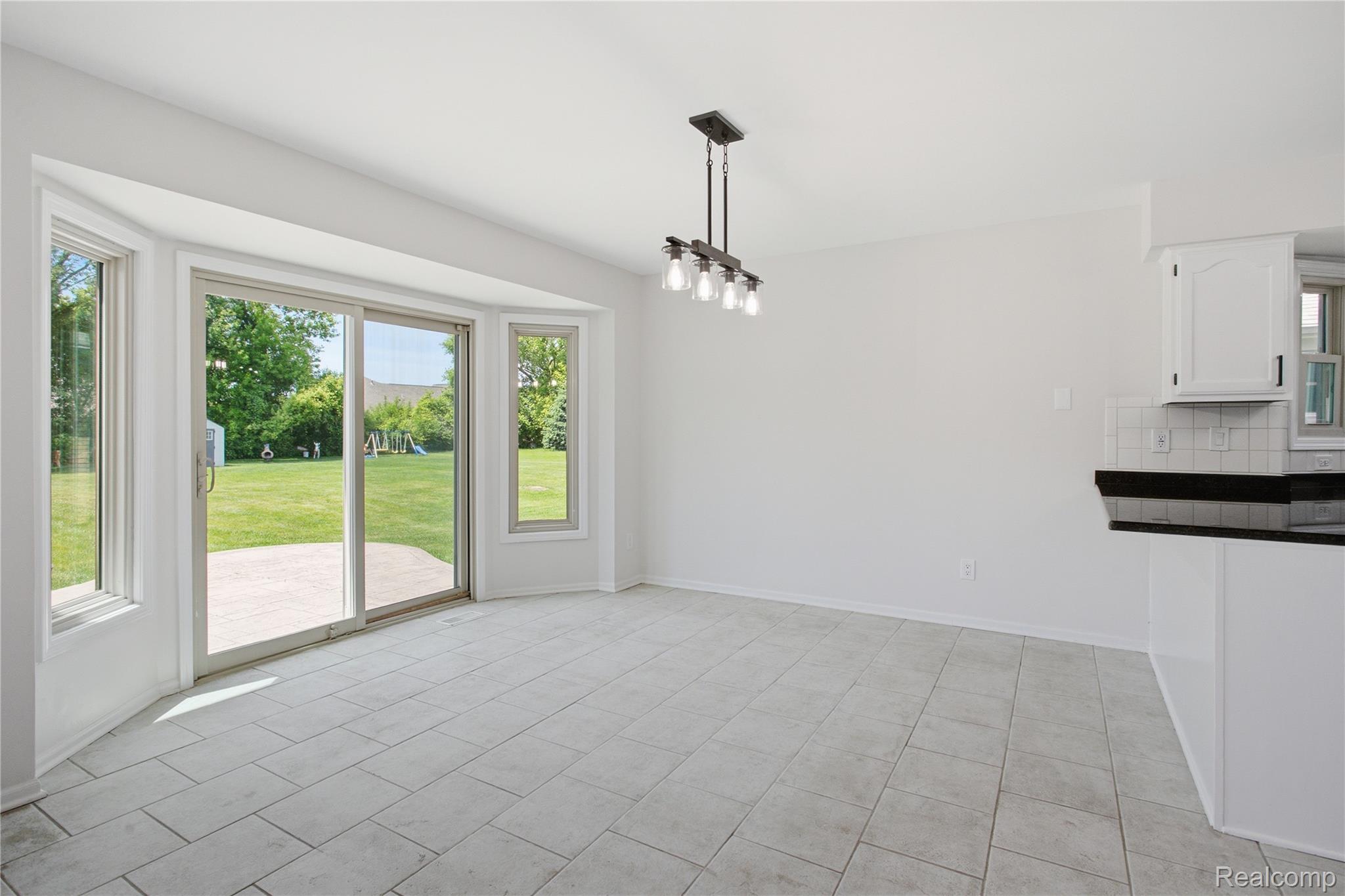 52658 Stag Ridge Drive Macomb, MI 48042 - Photo 12 of 28 Dining area featuring tile flooring, a bay window with a sliding glass door, a contemporary linear chandelier, and a partial view of kitchen cabinetry with a dark countertop and white subway tile backsplash