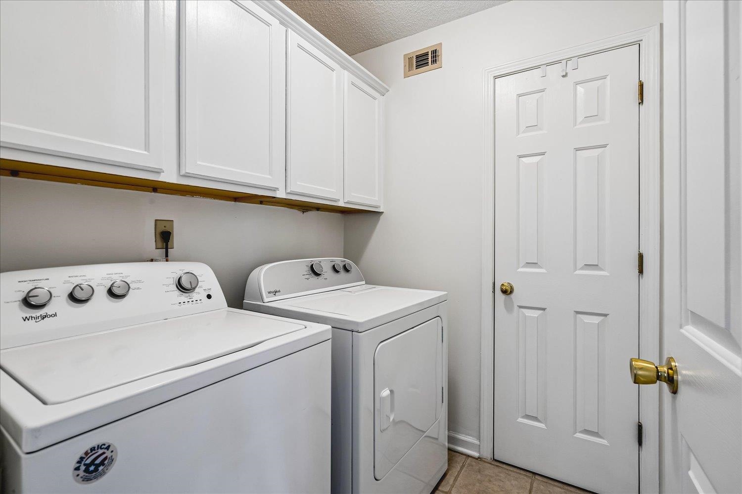 6335 Needle Ridge Road Bartlett, TN 38135 - Photo 14 of 25 Utility area featuring white paneled upper cabinetry, neutral-toned floor tile, and a four-panel interior door with brass hardware